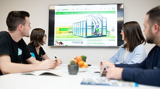 Eine Gruppe von Personen sitzt um einen Tisch und blickt auf einen Bildschirm