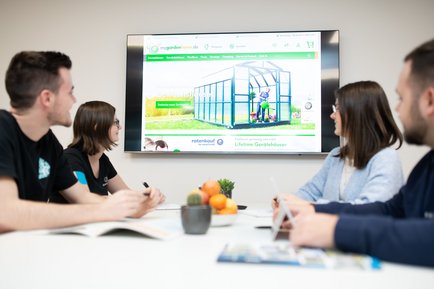 Eine Gruppe von Personen sitzt um einen Tisch und blickt auf einen Bildschirm