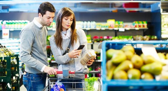 Ein Paar mit Einkaufswagen vor einem Obstregal schaut sich Informationen über ein Produkt auf ihrem Smartphone an.