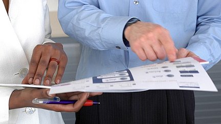 Zwei Personen halten eine Informationsmappe und zeigen auf die Inhalte.