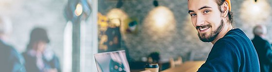 Ein junger Mann sitzt vor einem Laptop im Café