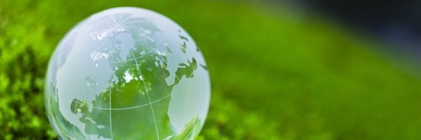 Eine Weltkugel aus Glas auf einer grünen Wiese symbolisiert Nachhaltigkeit