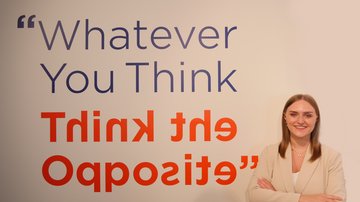 Frau steht vor einem Schriftzug: "Whatever You Think, Think the Opposite"