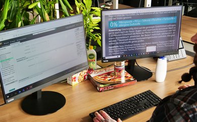 Mann am Schreibtisch vor zwei Bildschirmen beim Produktabgleich von Inhaltsangaben