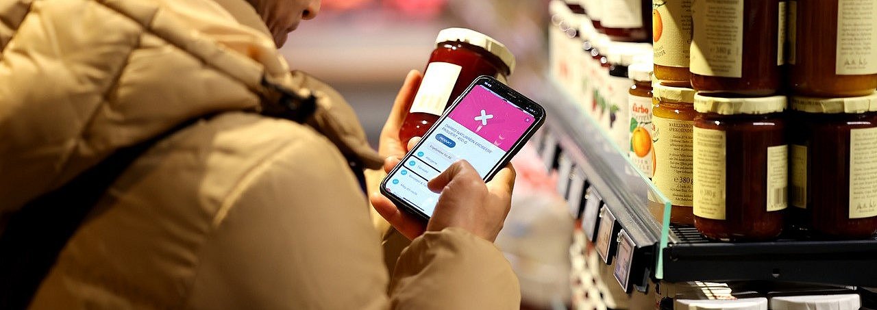 Ein Mann scannt mit der SoVi App auf seinem Handy im Supermarkt Marmelade.