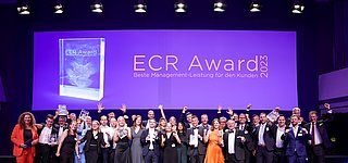 Gruppenbild der jubelnden Gewinnerteams vom ECR Award 2023 auf großer Bühne mit Trophäen