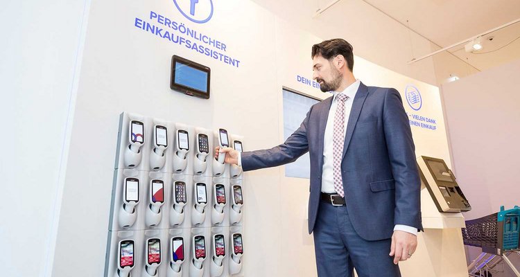 Fotografie Shopper Experience: Ein Kunde nimmt sich einen persönlichen Einkaufsassistent, mit dem wir selber unsere Einkäufe scannen und erfassen können.