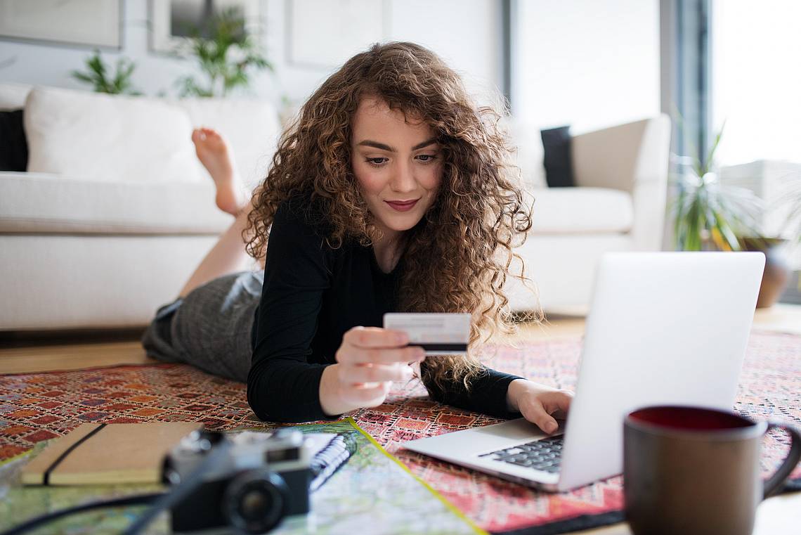 Frau vor Laptop beim Onlineshopping mit Kreditkarte in der Hand