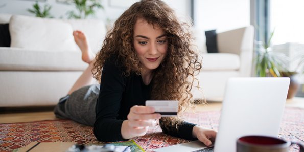 Frau vor Laptop beim Onlineshopping mit Kreditkarte in der Hand