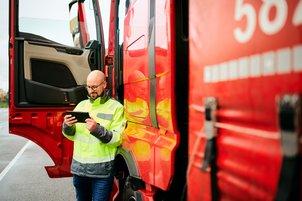 Fahrer steht neben LKW und schaut auf Handy