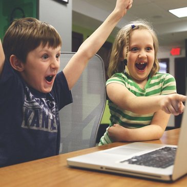 Bild: 2 Kinder sitzen fröhlich vor einem Laptop 