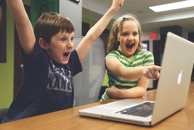 Bild: 2 Kinder sitzen fröhlich vor einem Laptop 