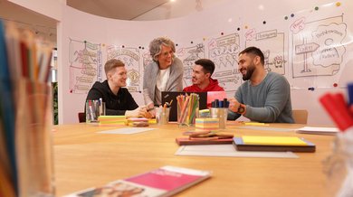 Frau diskutiert als Mentorin mit drei jungen Menschen über die Arbeitsergebnisse