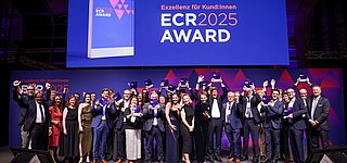 Gruppenbild der jubelnden Gewinnerteams in eleganter Abendgarderobe vom ECR Award 2025 auf großer Bühne mit Trophäen