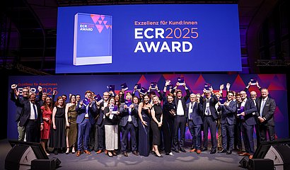 Gruppenbild der jubelnden Gewinnerteams in eleganter Abendgarderobe vom ECR Award 2025 auf großer Bühne mit Trophäen