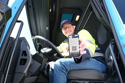 Fahrer zeigt aus LKW-Kabine digitalen Lieferschein auf Smartphone