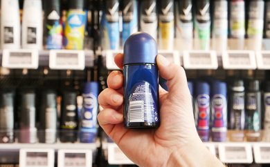Deoroller in der Hand eines Mannes vor einem Regal mit der Ansicht auf die Inhaltsstoffe der Rückseite