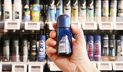 Deoroller in der Hand eines Mannes vor einem Regal mit der Ansicht auf die Inhaltsstoffe der Rückseite