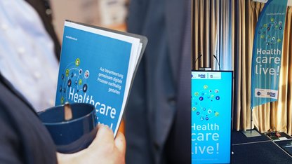 Fotokollage aus Programmflyer tragende Person und Healthcare live gebrandetes Rednerpult 