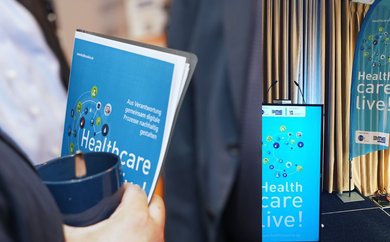 Fotokollage aus Programmflyer tragende Person und Healthcare live gebrandetes Rednerpult 
