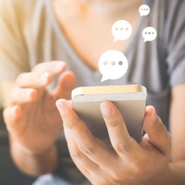 Eine Frau hält ein Smartphone in der Hand. Textblasen symbolisieren eine laufende Unterhaltung.
