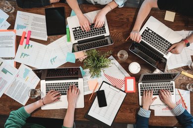Eine Gruppe von Menschen sitzen an ihren Laptops rund um einen Tisch
