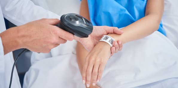 Im Krankenhaus scannt ein Arzt einer Patienten das Bändchen am Arm