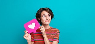 Eine junge Frau hält eine Sprechblase mit einem Herz hoch