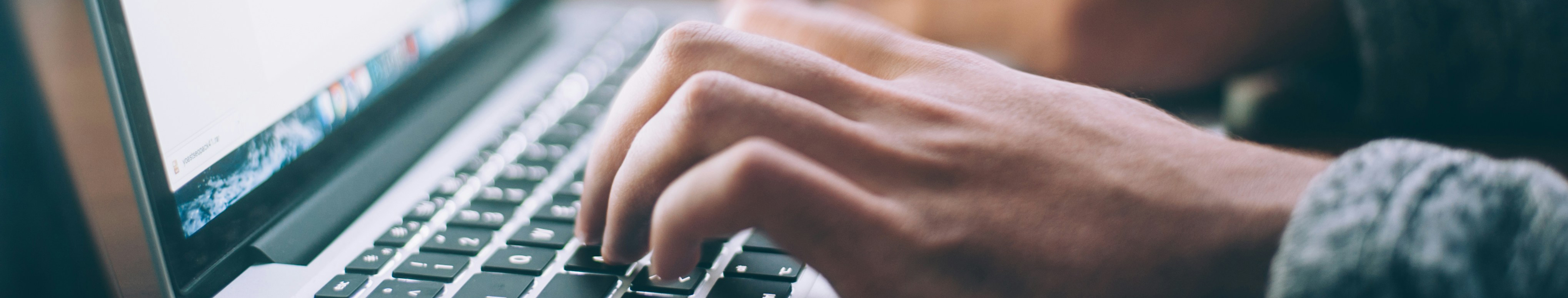 Mann tippt auf Computertastatur, was den Versand/ Empfang/ Bearbeitung einer E-Rechnung simulieren soll 